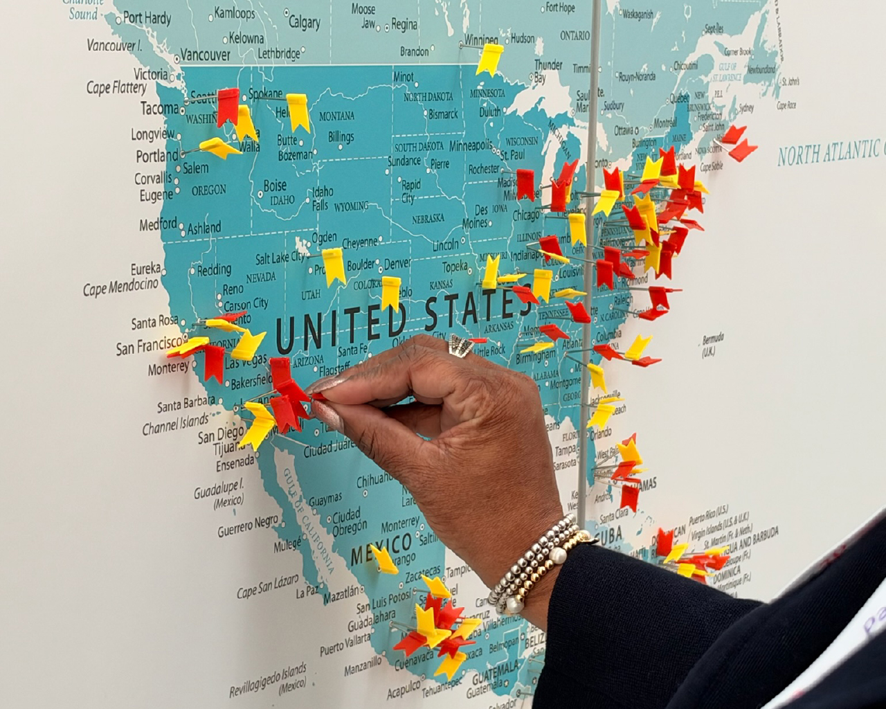 A close-up view of hands placing colorful pushpins onto a large world map display.