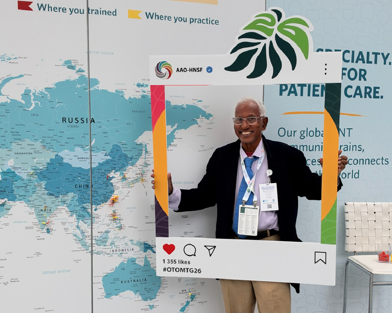 A man standing in a convention hall holding up a large, social-media-style photo frame cutout while smiling for the camera.